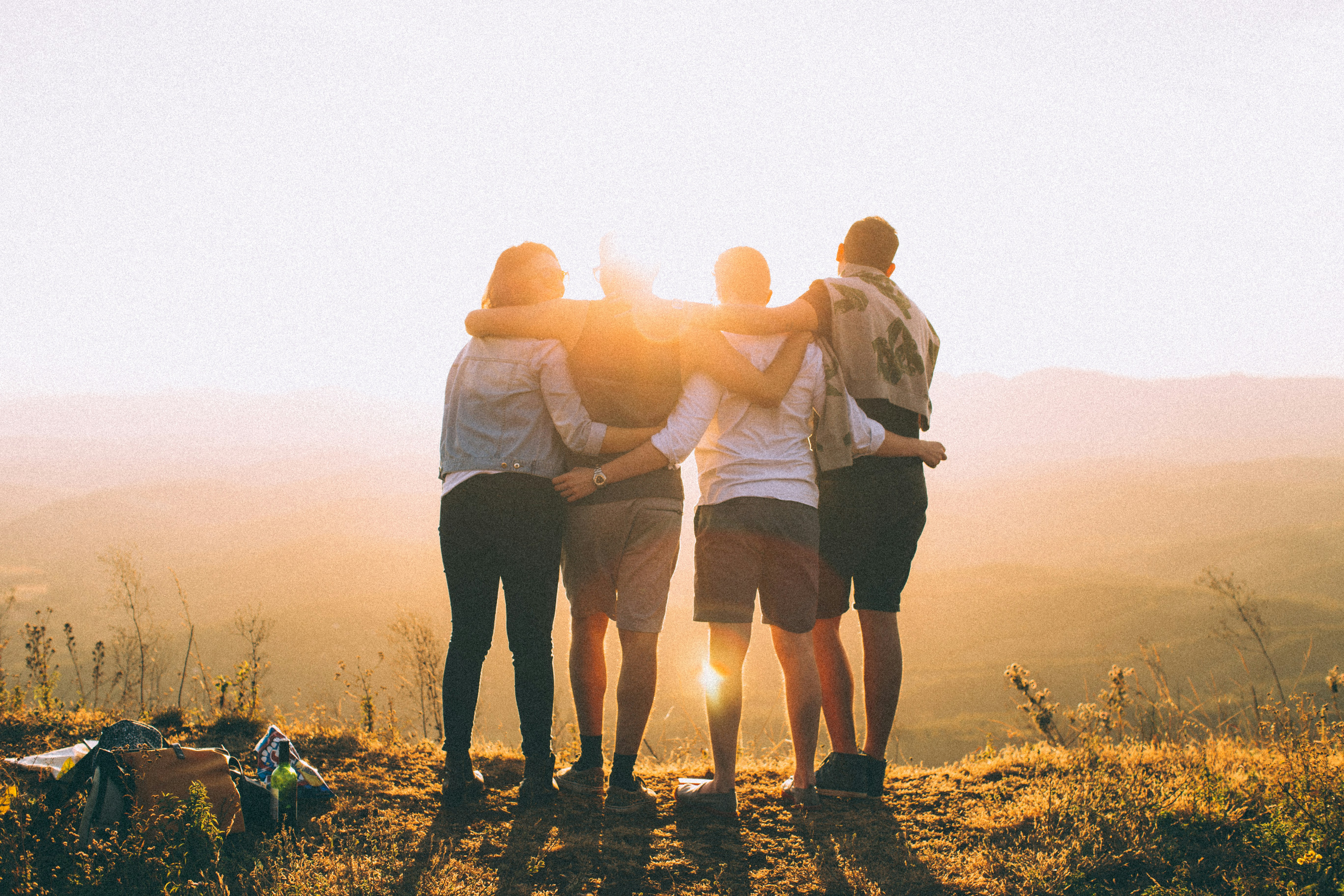 Friends stand on a hill, silhouetted against a vibrant sunset